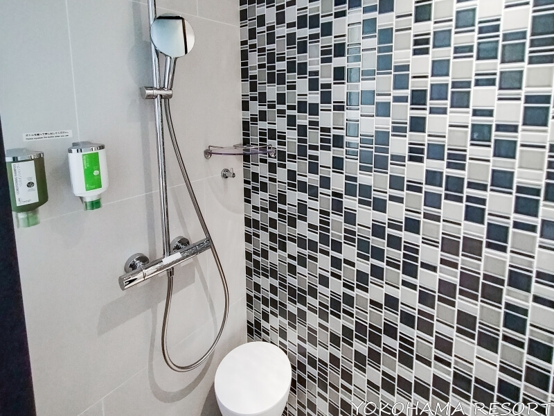 シャワーブースに白い腰かけとシャンプー類が壁に備え付け、ハンドシャワー