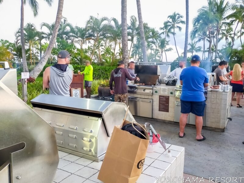 夕方BBQコンロに大勢の人が集まって食材を焼いている