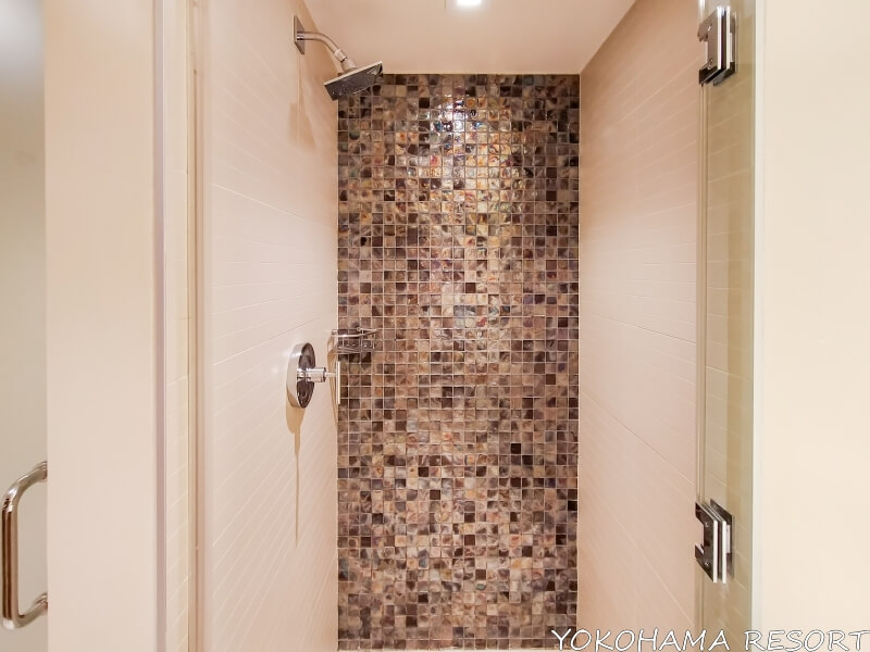 固定式シャワーのみのシャワーブースの壁はブラウン系のモザイクのようなタイル