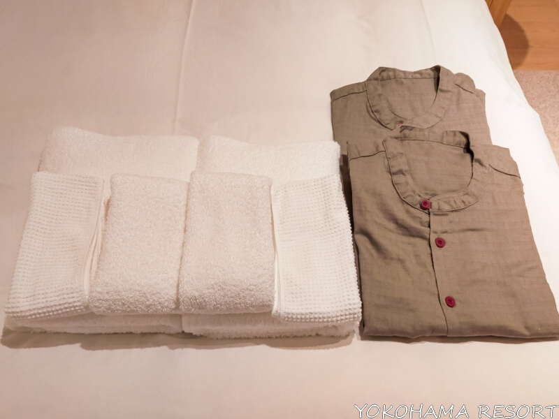 ベッドの上に置いてある白いタオルとブラウンのルームウェアが二人分