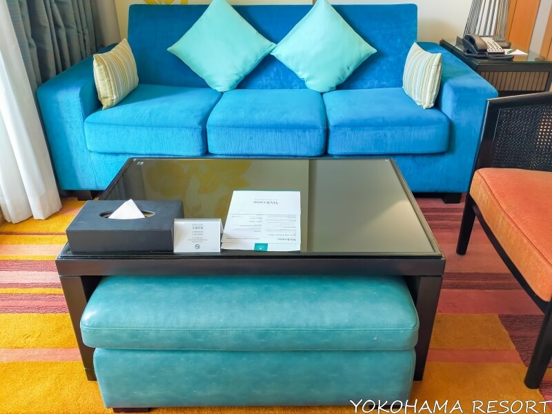 リビングに青い大きなソファーと四角いローテーブル、その下にオットマン