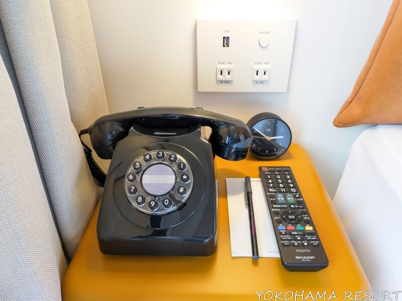 プッシュ式の黒電話、黒く丸い小さいアナログ時計、TVリモコン、メモ帳とペン